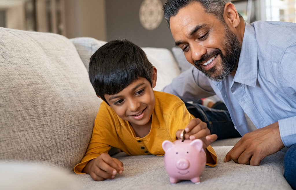 Father with son on the sofa putting coins into a piggy bank