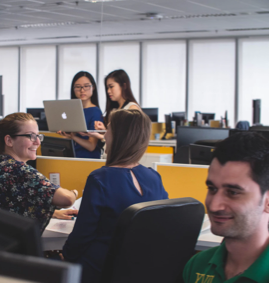 Inside the office with workers speaking to each other looking at computer screens