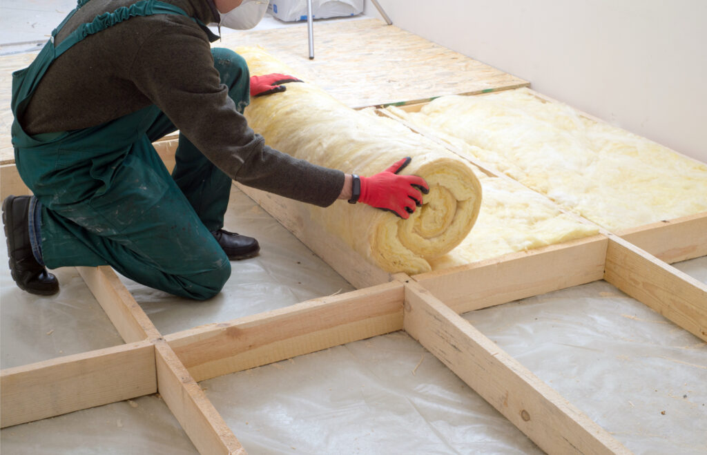 Workman rolling out rolls of insulation on a floor