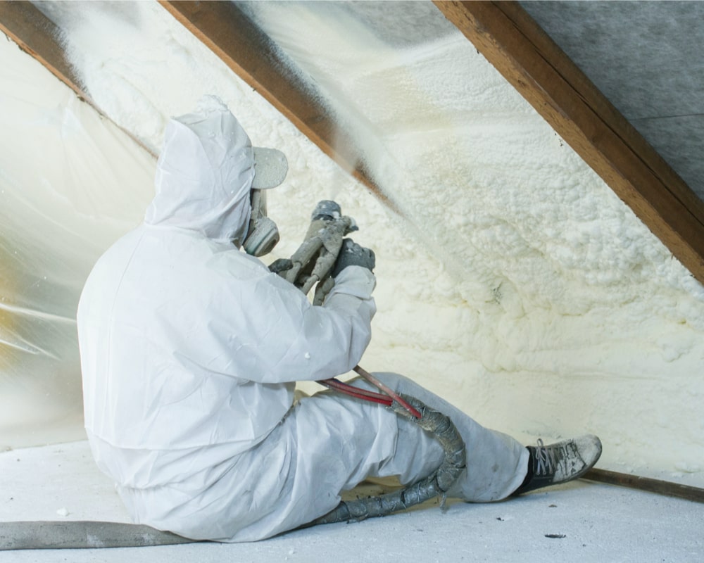 Installer spraying spray foam insulation into loft rafter wearing a hazmat suit